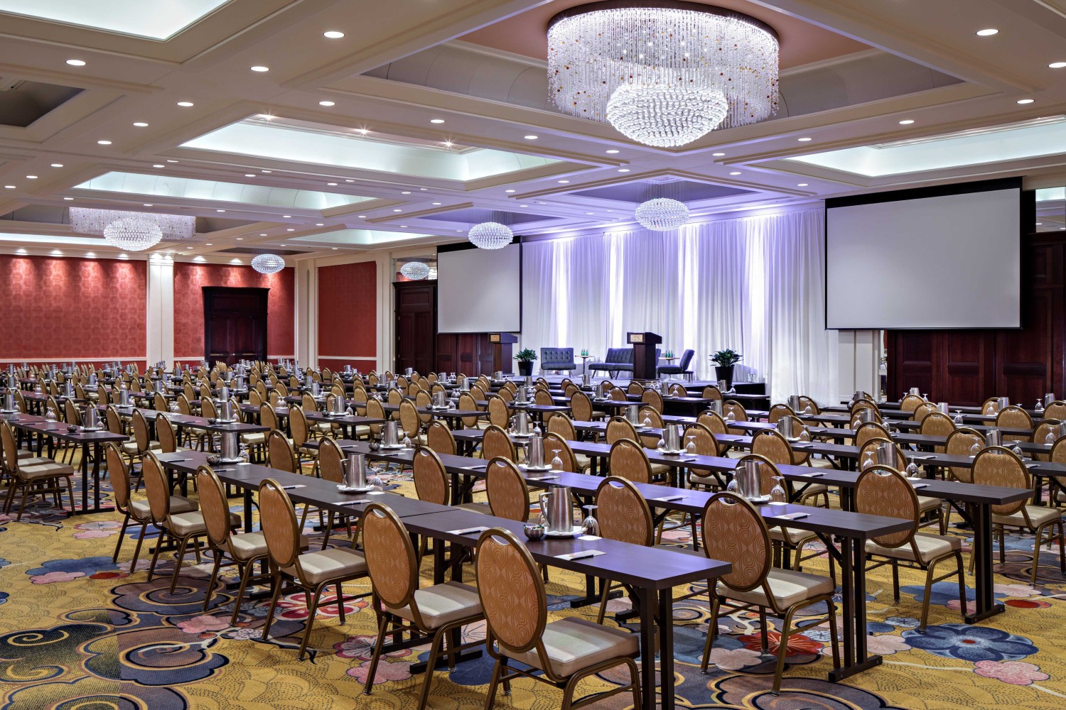 Amway Grand_Ambassador Ballroom_Ballroom_Meeting Room_Event Space_Set Up_Rows of Tables_Chairs_Projector Screens_Chandeliers_Notepads_Pens_Stage_Podium
